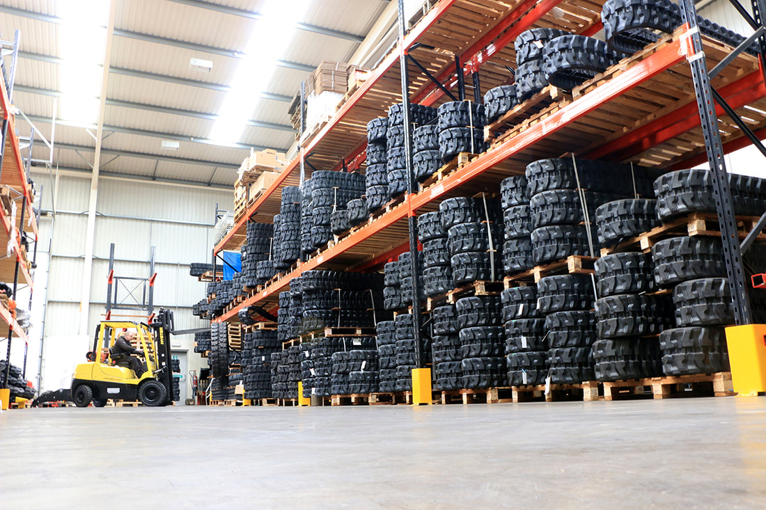 Picture of the mini excavator rubber tracks section of the DIGBITS warehouse showing racks of tracks and a forklift loading.